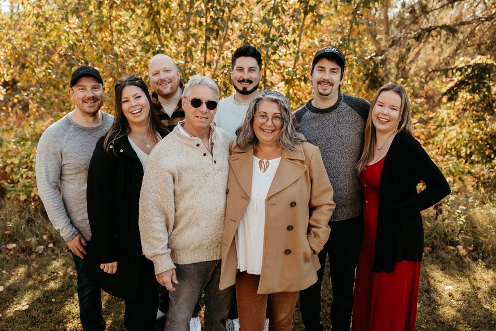Extended family gathering outdoors for a group photo with autumn foliage in the background.