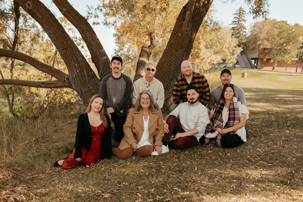 Family group sitting together under large autumn trees during outdoor photo session.