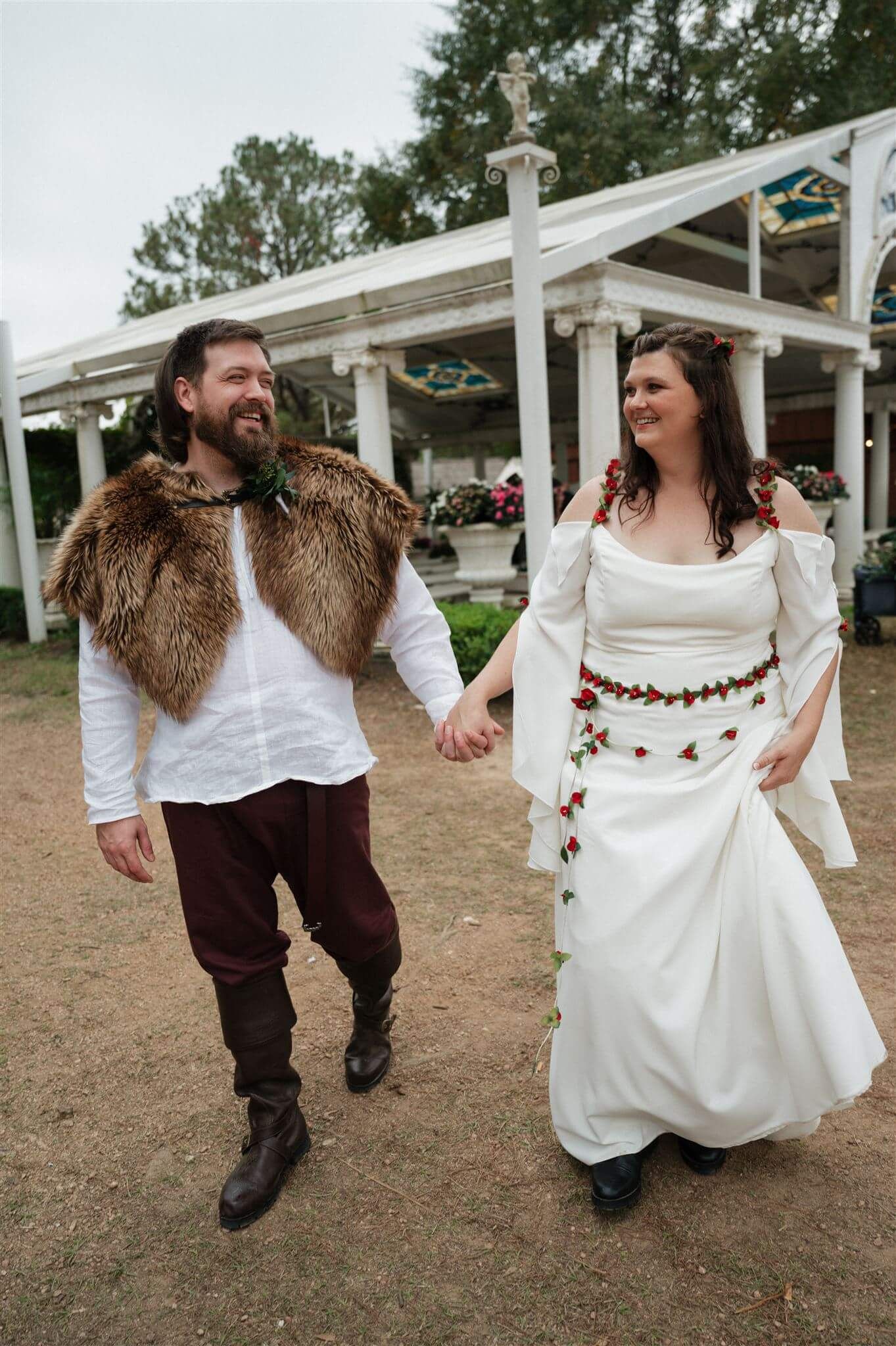 Couple in medieval attire walking and laughing together under white pergola structure.