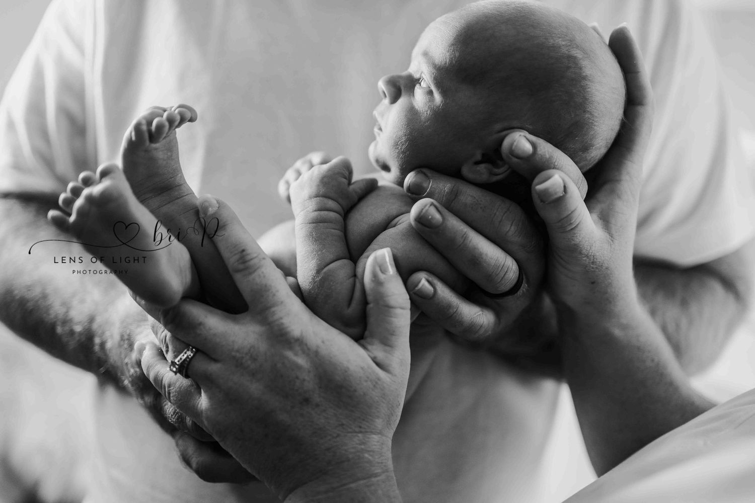A tender black and white image of hands gently cradling a newborn baby.