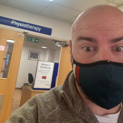 A person wearing a black face mask at a physiotherapy clinic entrance.