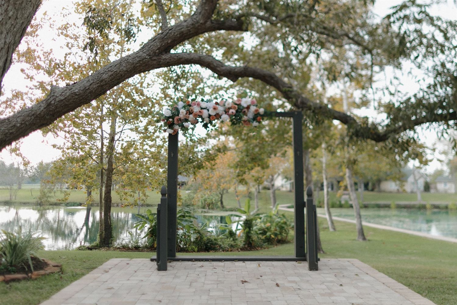 Elegant black metal wedding arch set up by a lake with trees in the background.