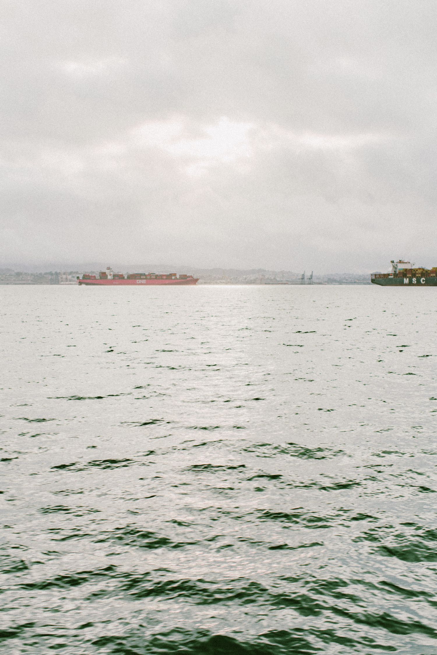 Red cargo ship sailing on choppy waters under overcast skies.