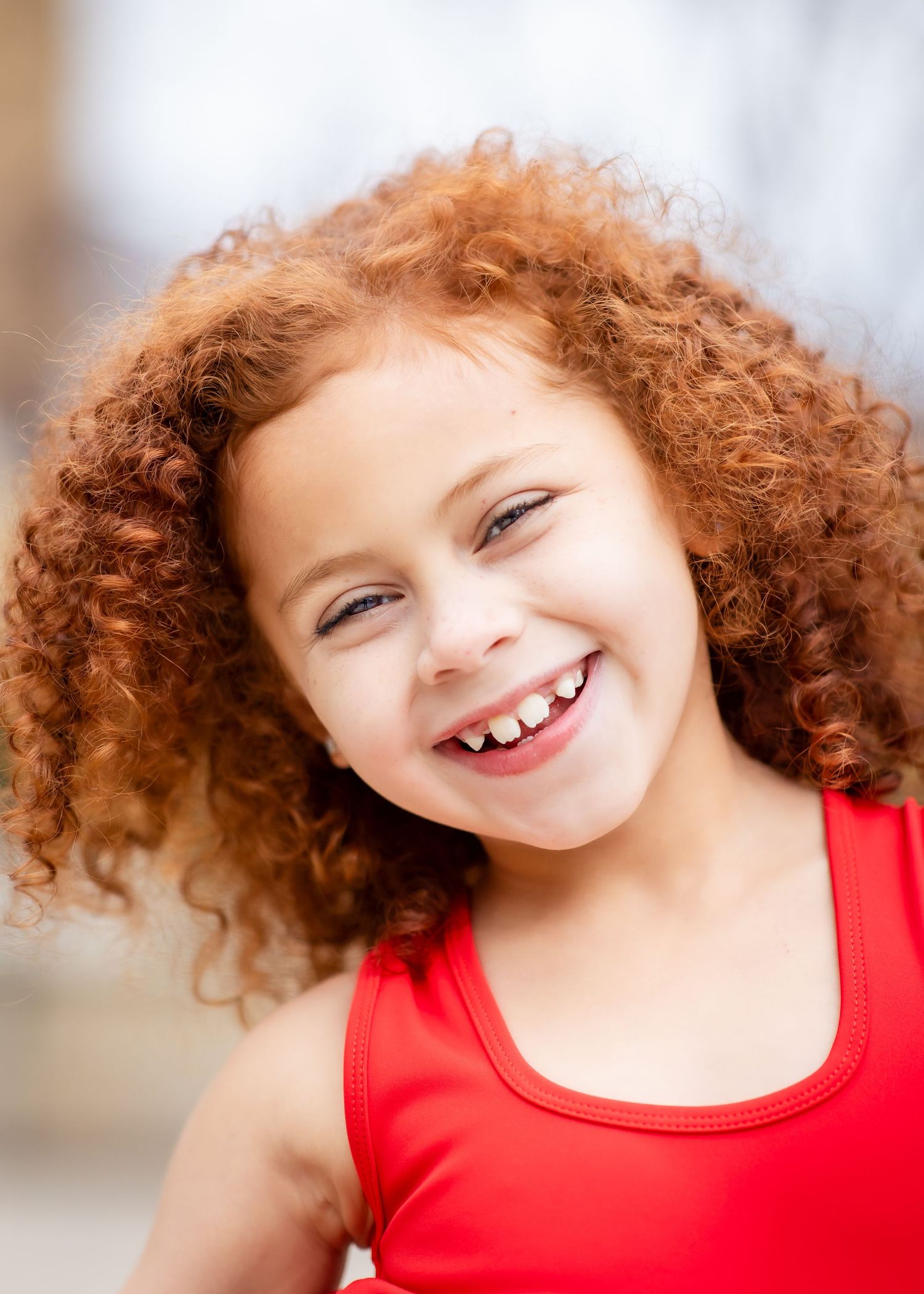 Portrait of a happy child with natural curly red hair wearing a red tank top.