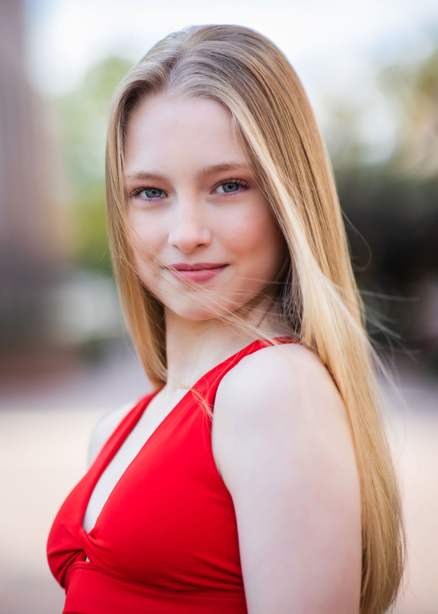 Portrait in natural lighting wearing a red dress against a soft blurred background.
