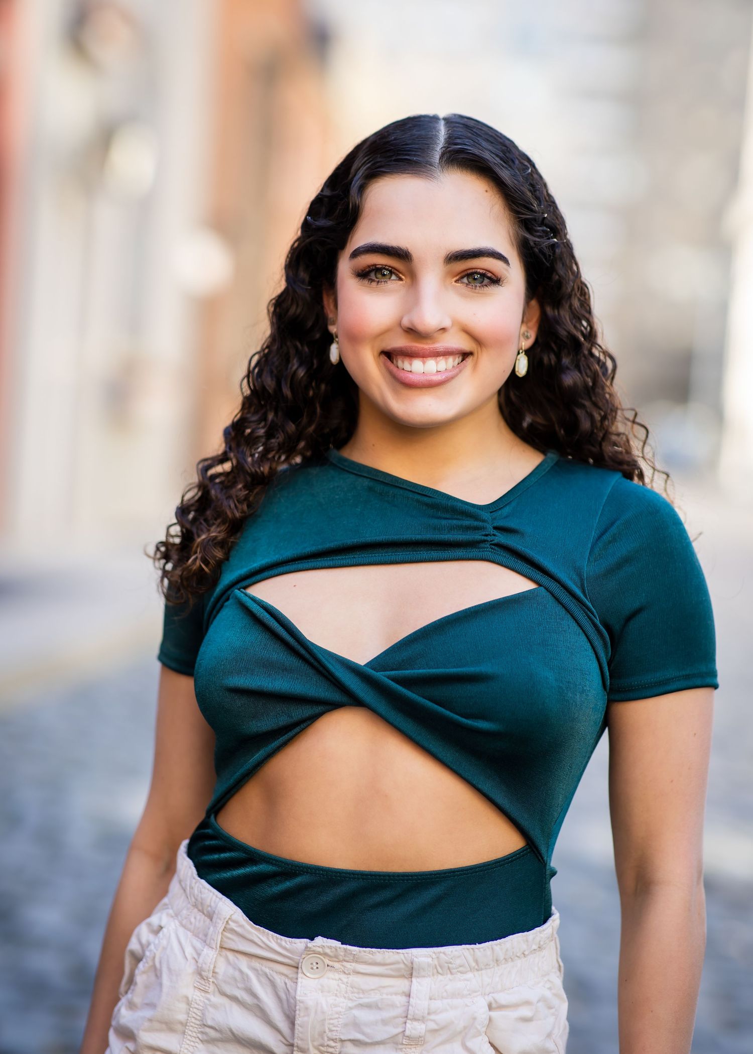 Portrait featuring dark curly hair and emerald green top with modern cutout design.