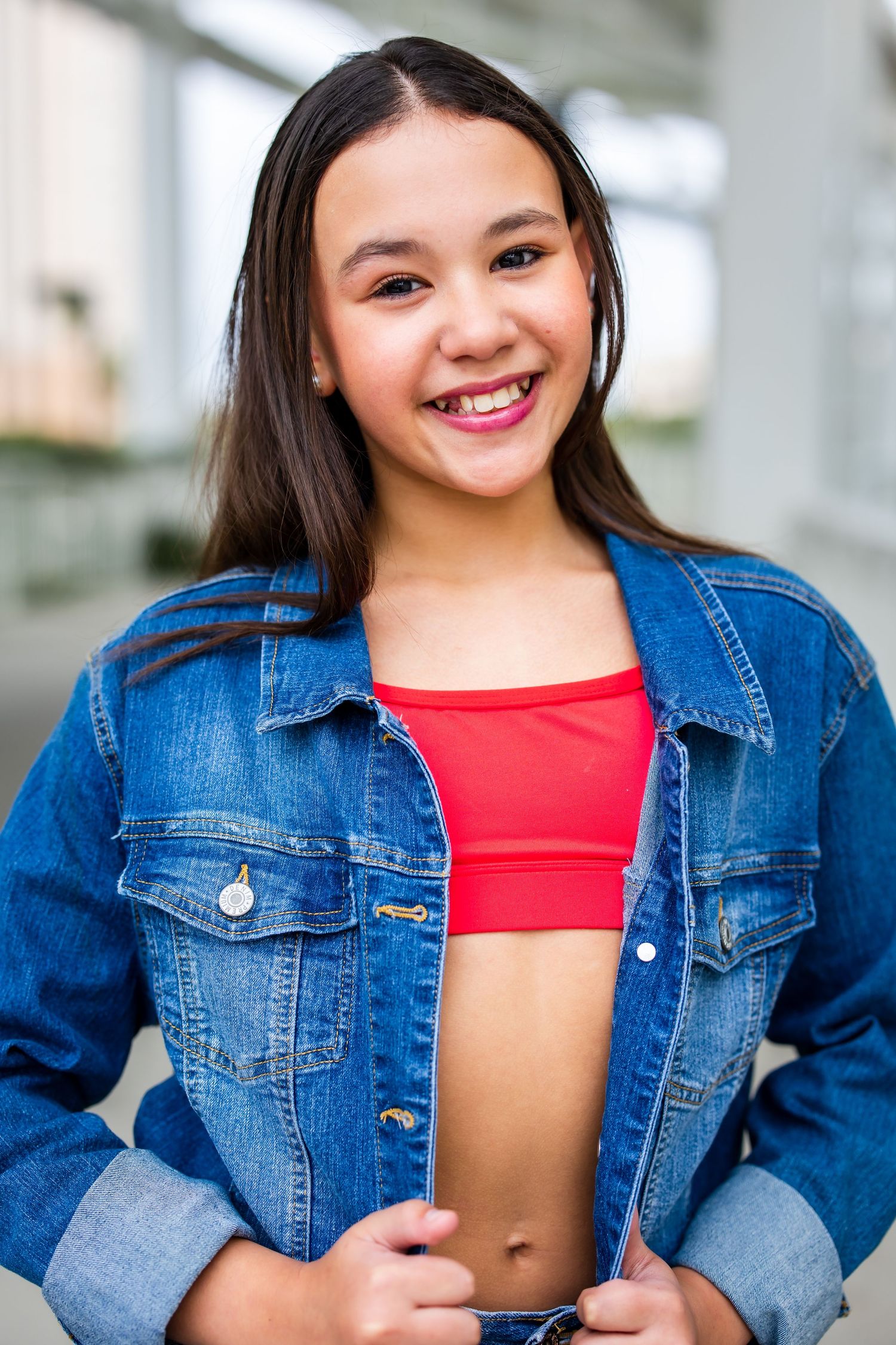 Athletic young woman in denim jacket and red crop top smiles brightly outdoors.