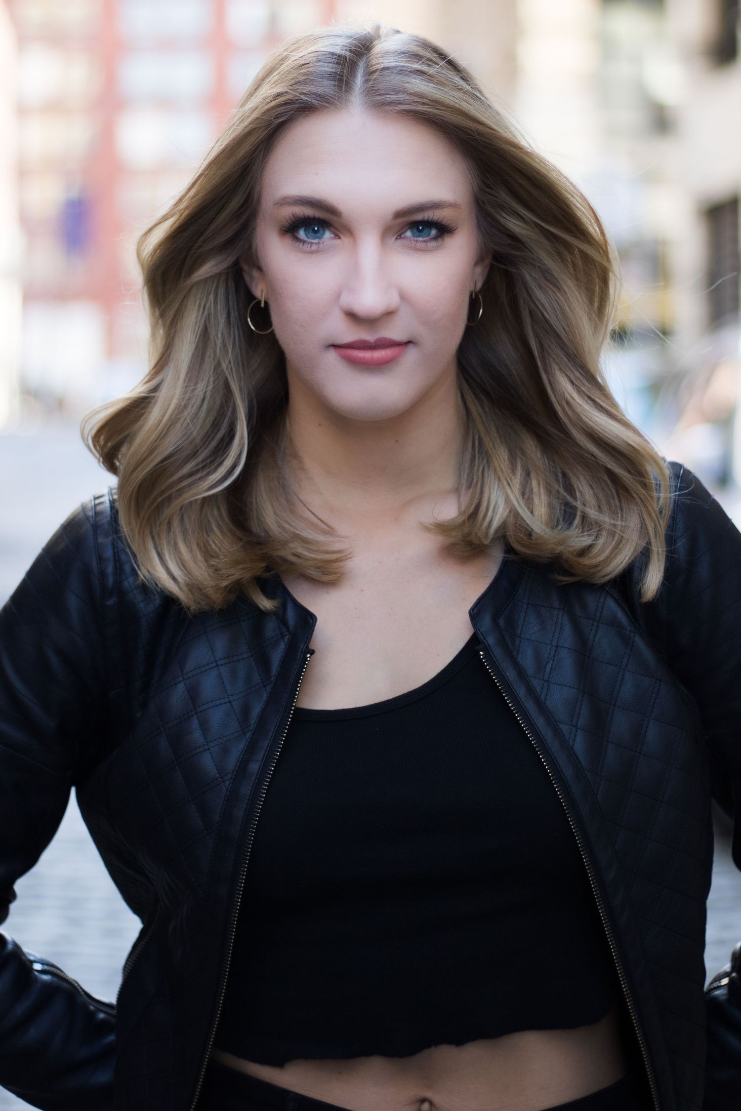 Portrait of a person wearing a black leather jacket and crop top against an urban background.