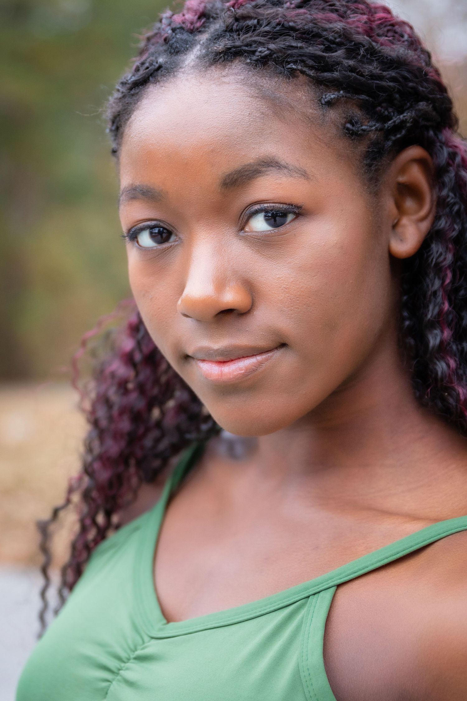 Portrait of a person with burgundy braids wearing a green tank top.