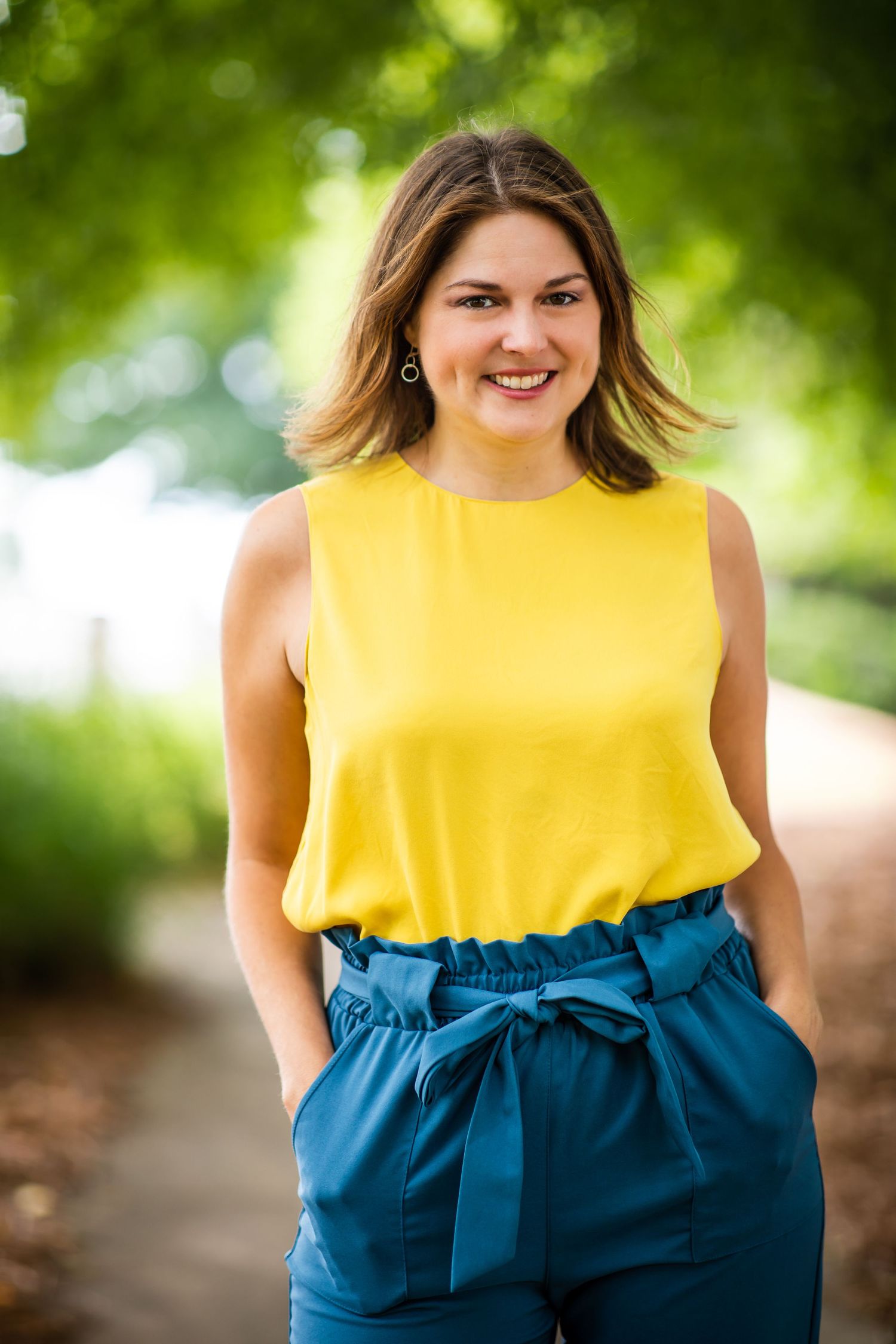 Portrait of someone in yellow sleeveless top and blue pants outdoors.