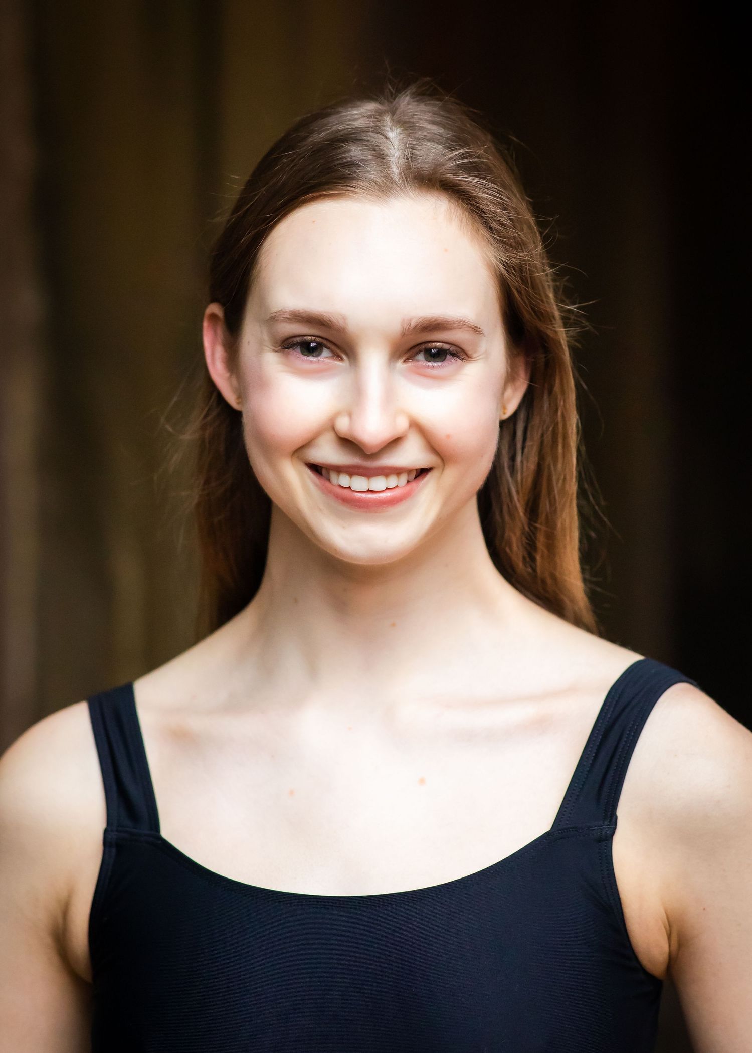A close-up headshot portrait showing a warm smile against a dark background.
