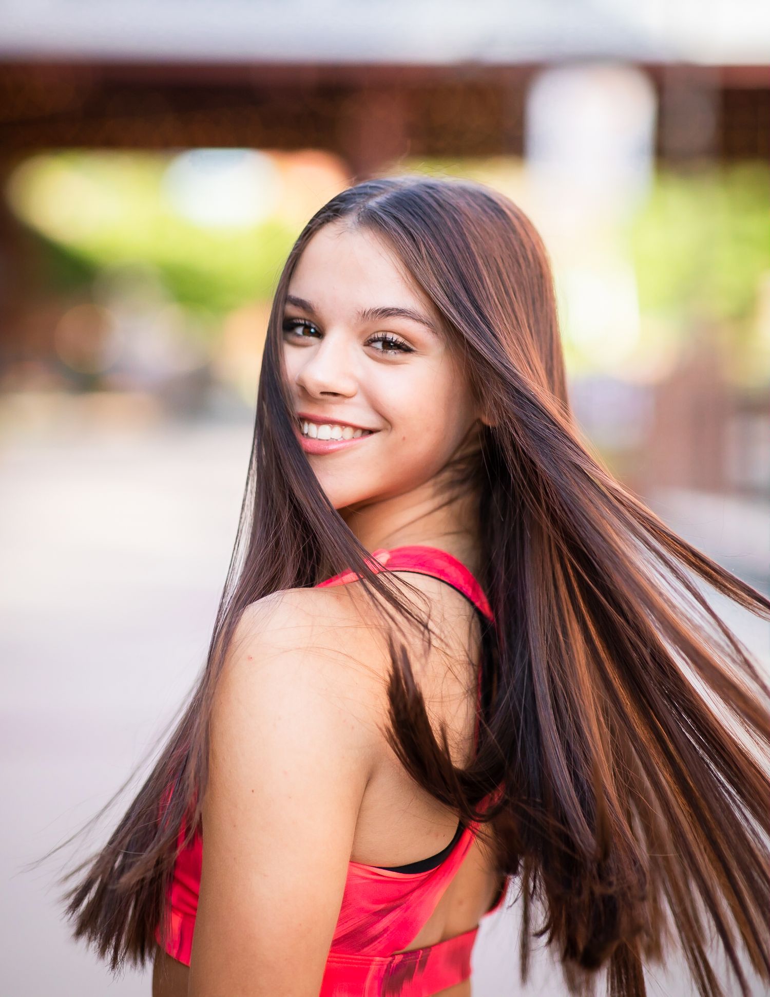 Portrait of a person in a red top with long straight hair turning to smile at the camera.