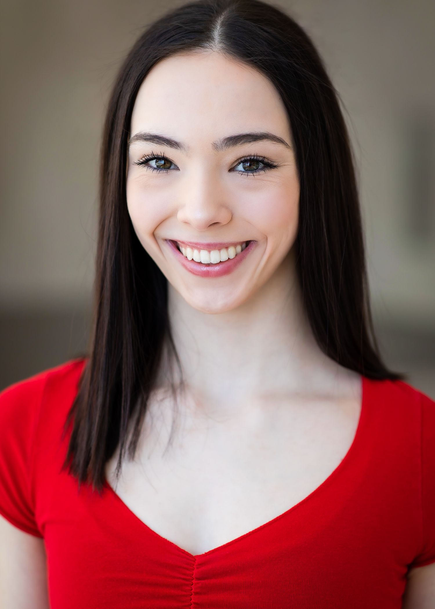 Portrait in red v-neck top with dark hair and bright smile.