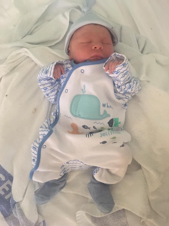 Newborn baby wearing white outfit with whale design sleeping peacefully.