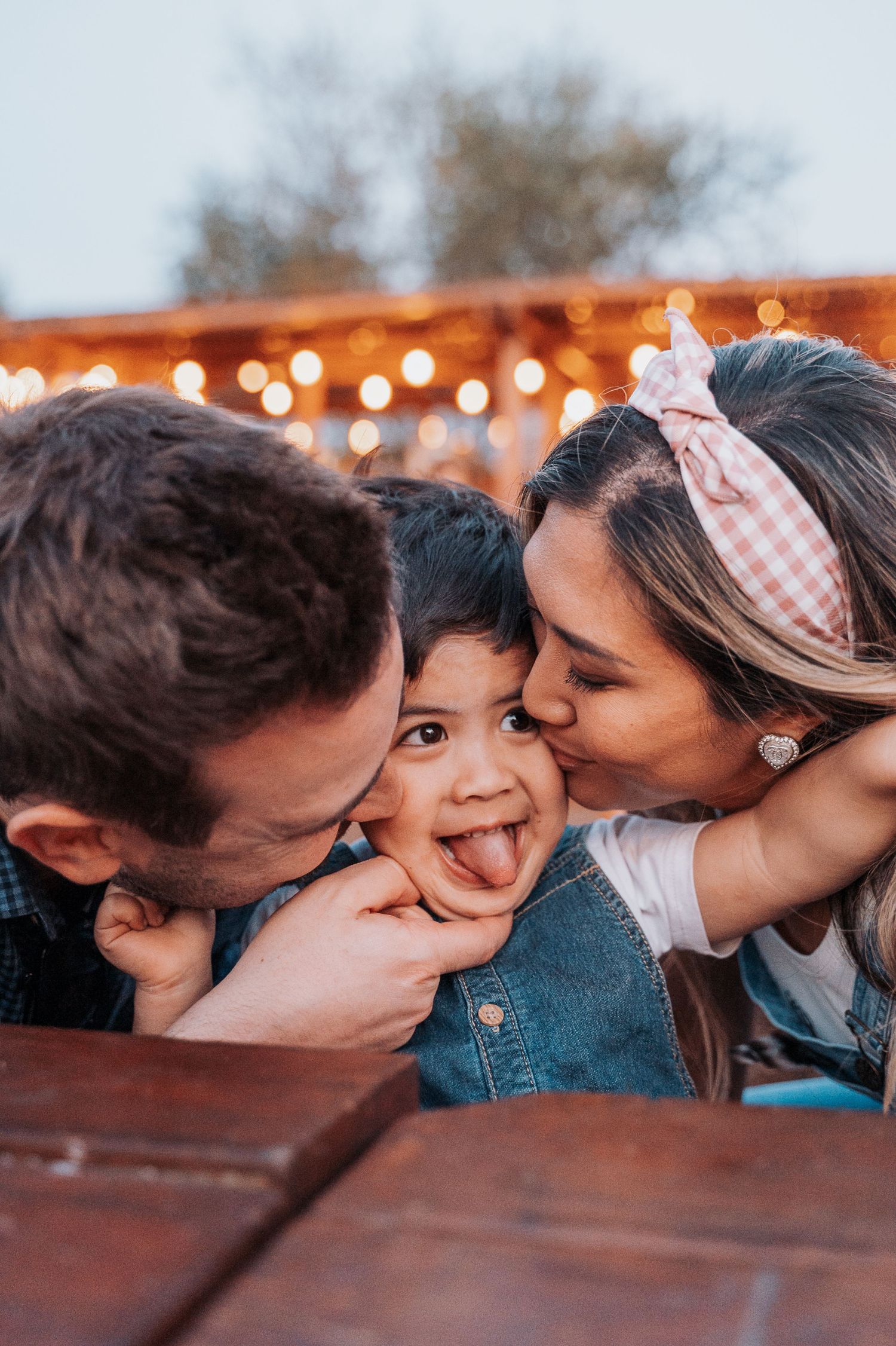 Family sharing affectionate kisses with string lights glowing in the background.