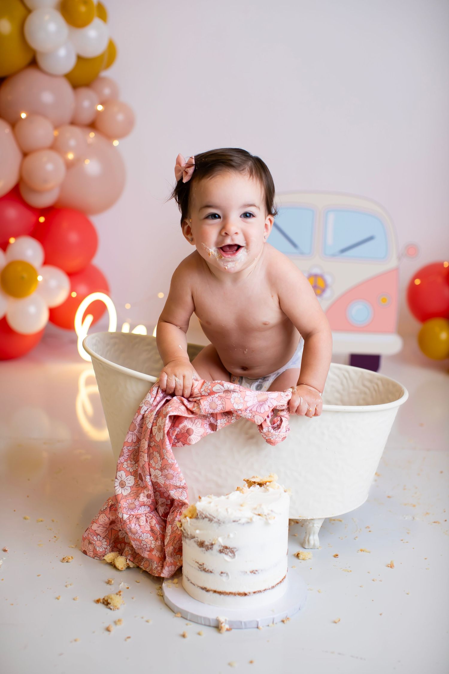 Joyful cake smash photo with white bathtub and festive balloon arch backdrop.