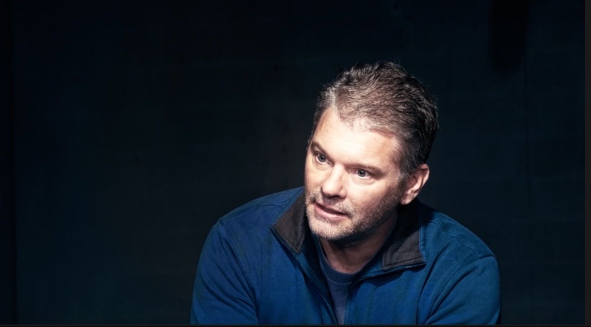 Dramatic portrait of person in blue shirt against dark background.