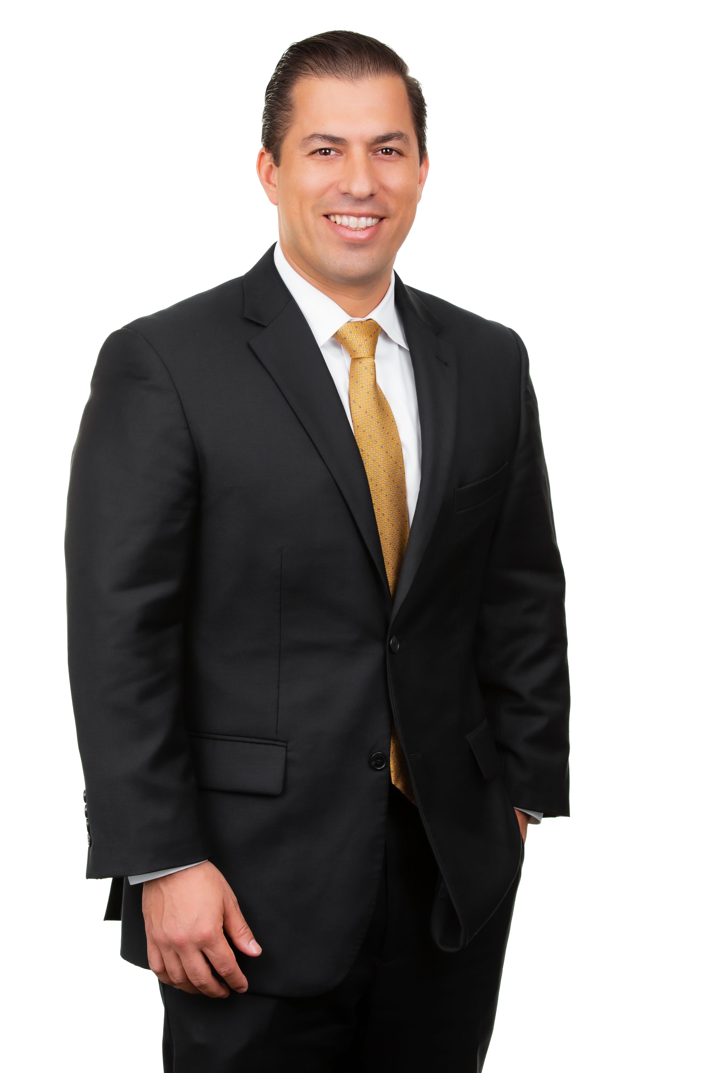 Business professional in dark suit and gold tie poses confidently against white backdrop.
