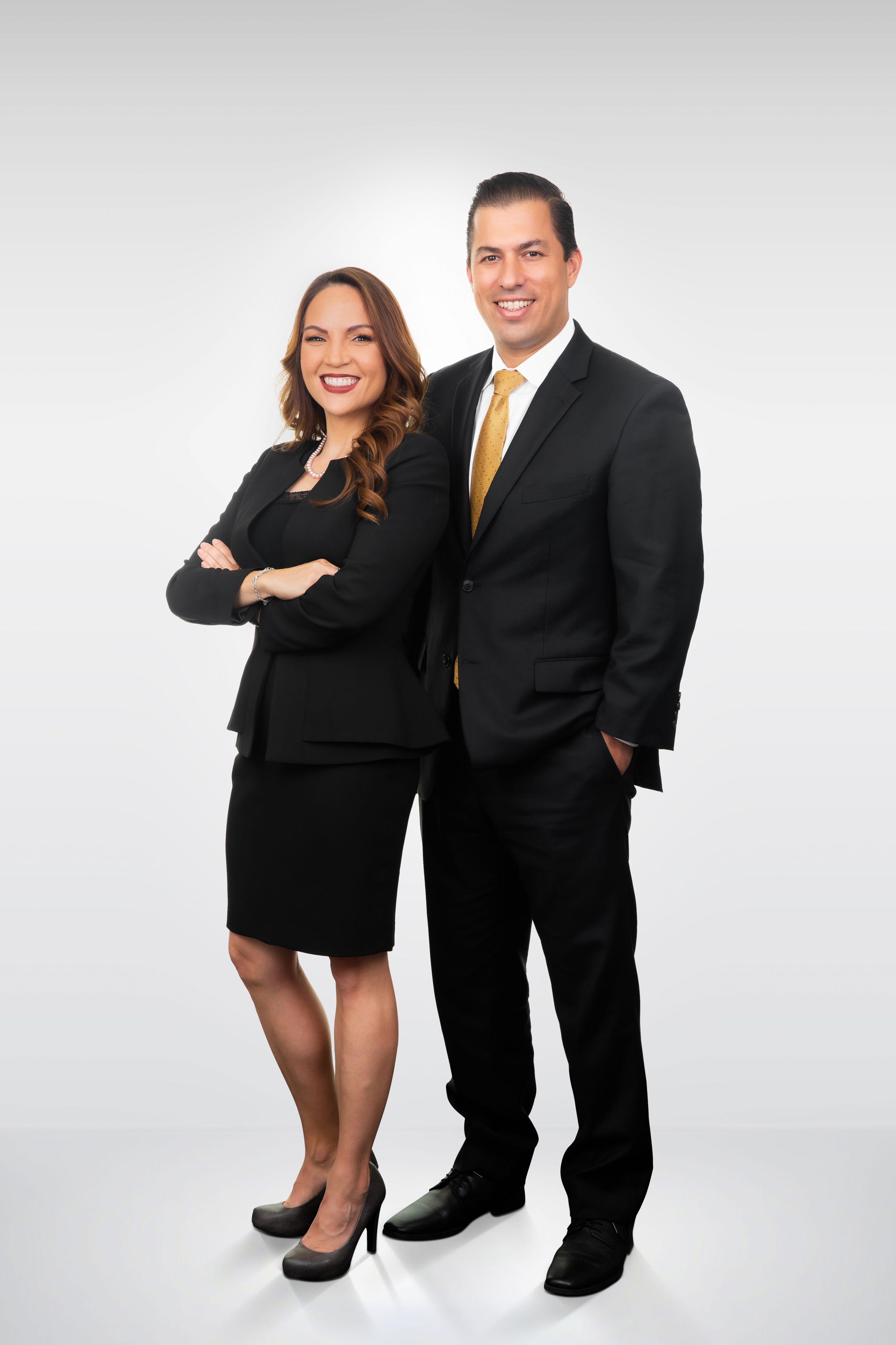 Business professionals in formal wear pose together in studio setting.