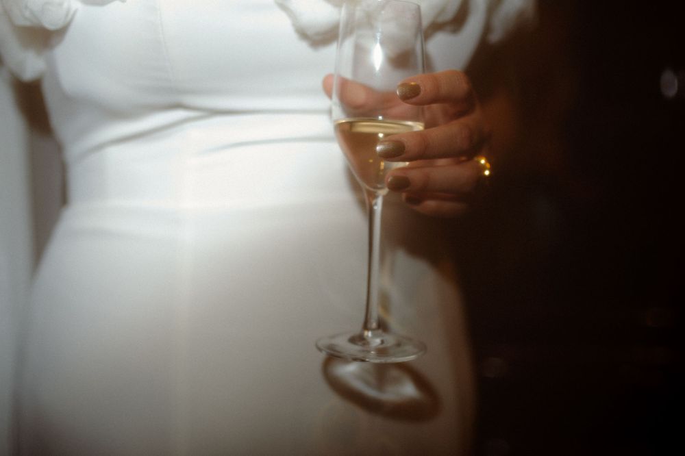 Close-up shot of hands holding a champagne flute against a white wedding dress.