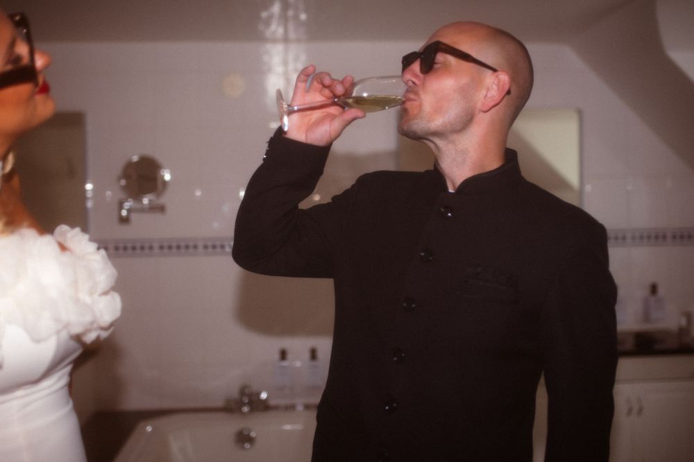 Person in black shirt takes a drink while celebrating in bathroom.