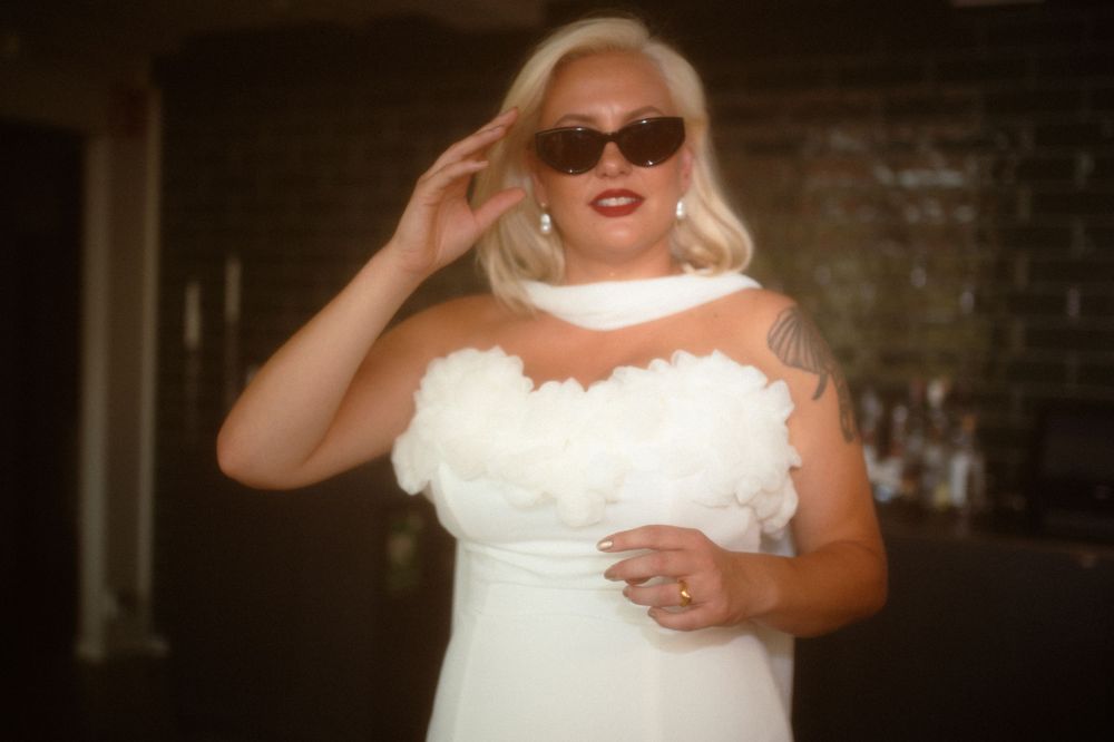 Bride in white dress and sunglasses poses with vintage glamour style.