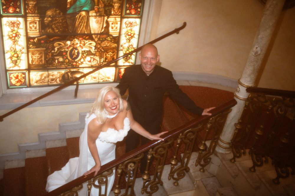 Wedding couple poses on vintage staircase with stained glass windows.