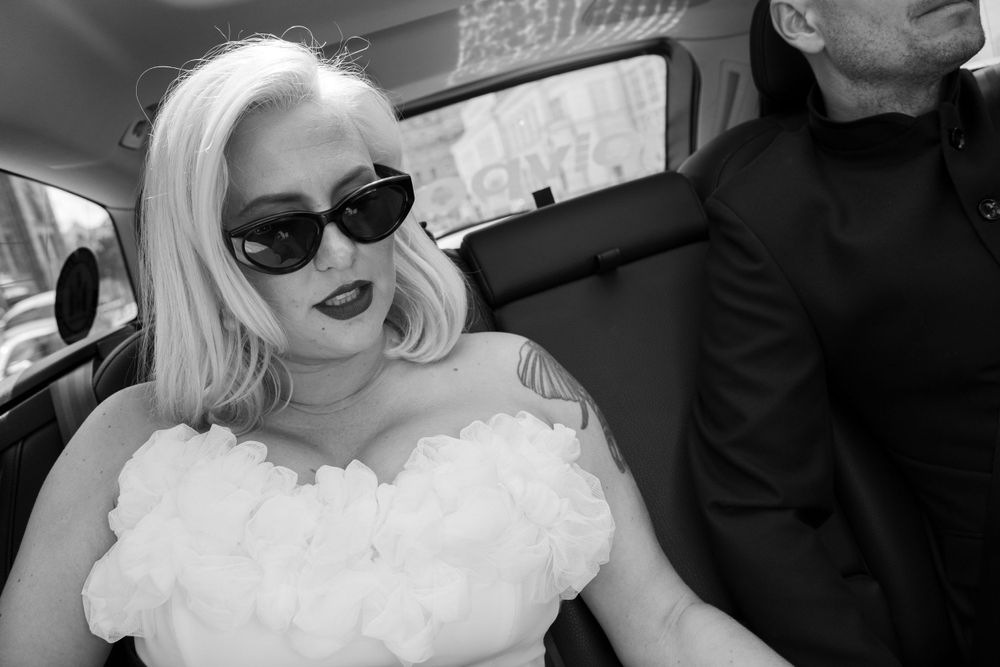 Stylish bride wearing sunglasses in black and white portrait inside car.