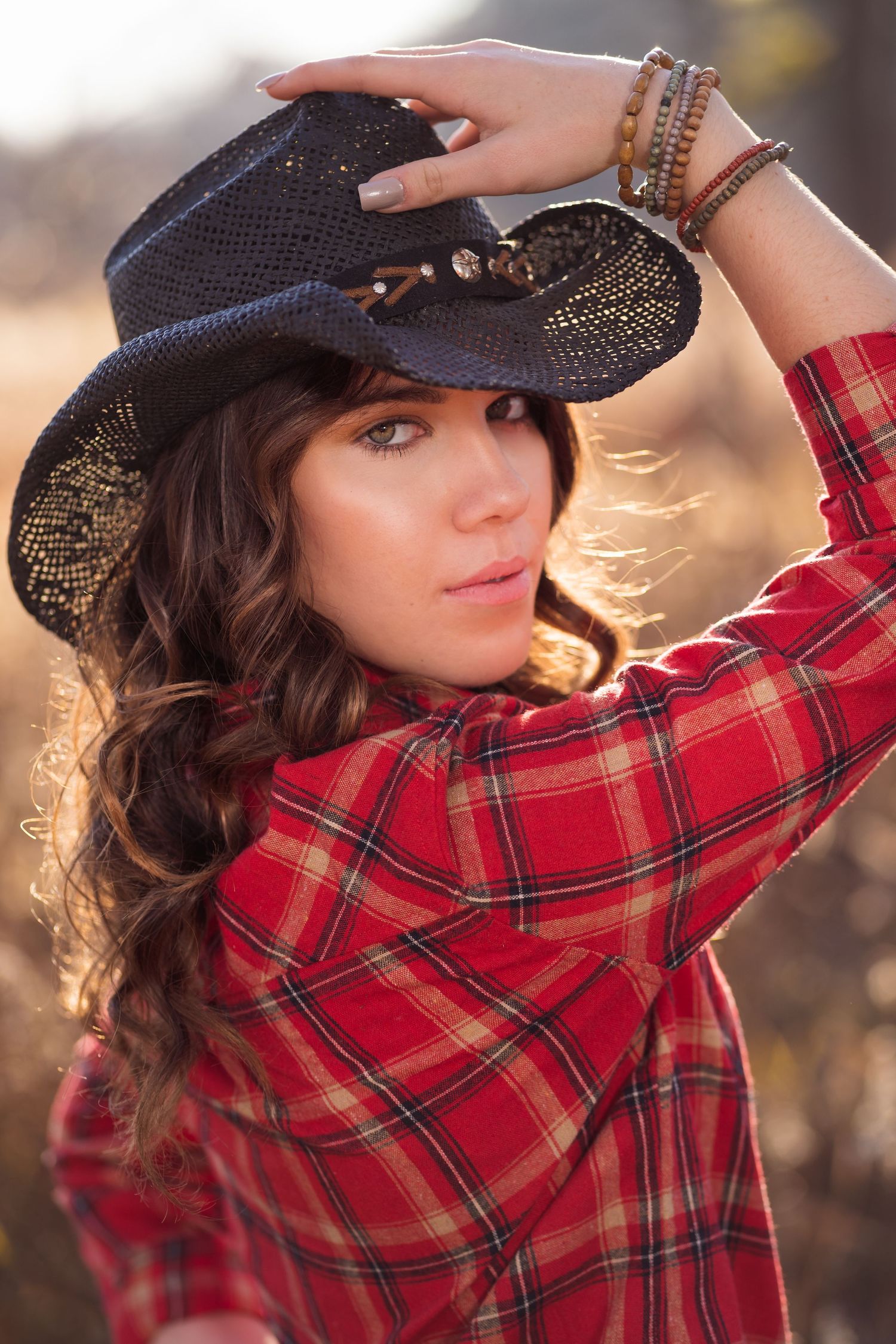 Woman in a red plaid shirt and black hat poses playfully in a series of outdoor portraits at sunset.