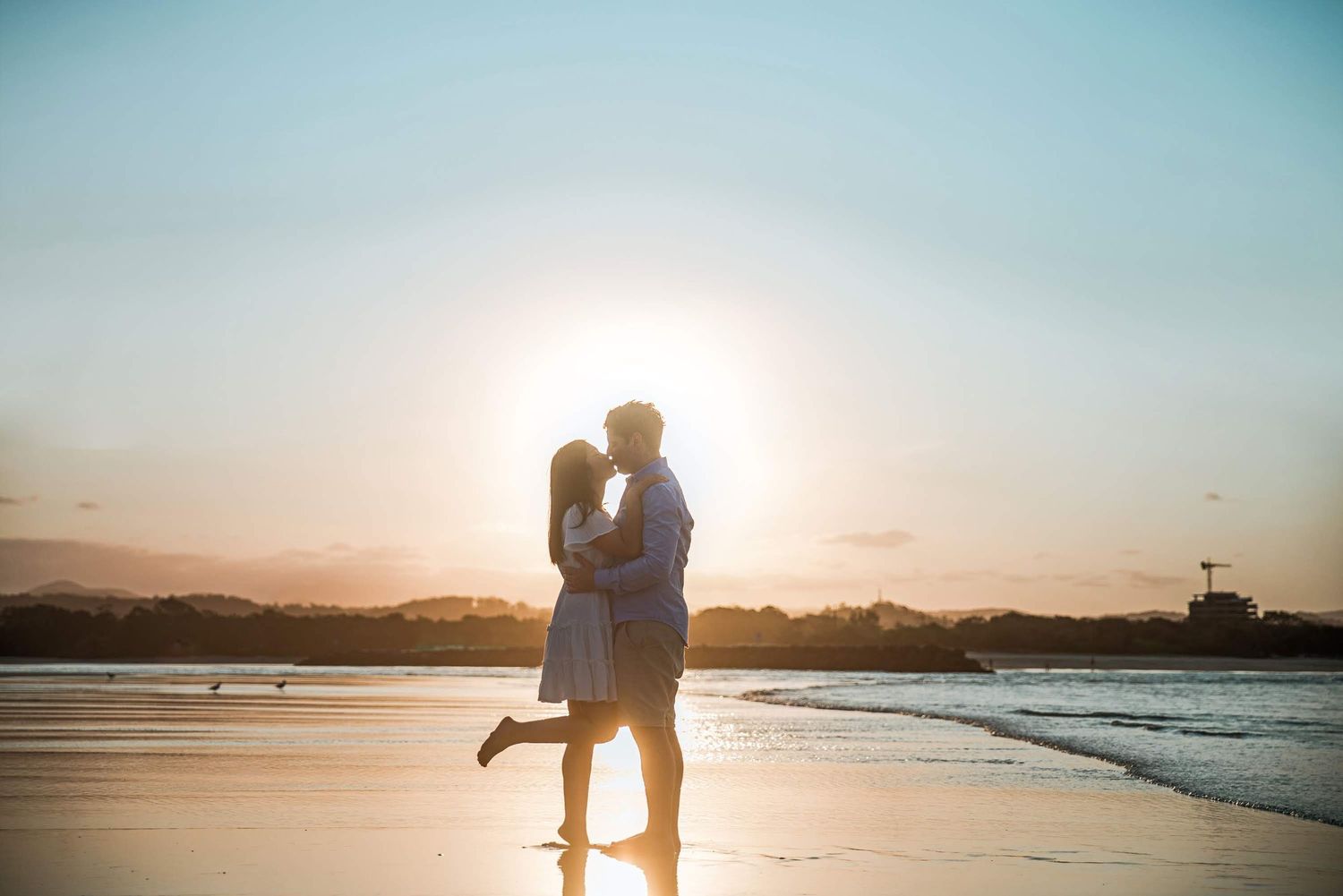 Silhouetted couple embracing on beach at sunset with ocean in background.