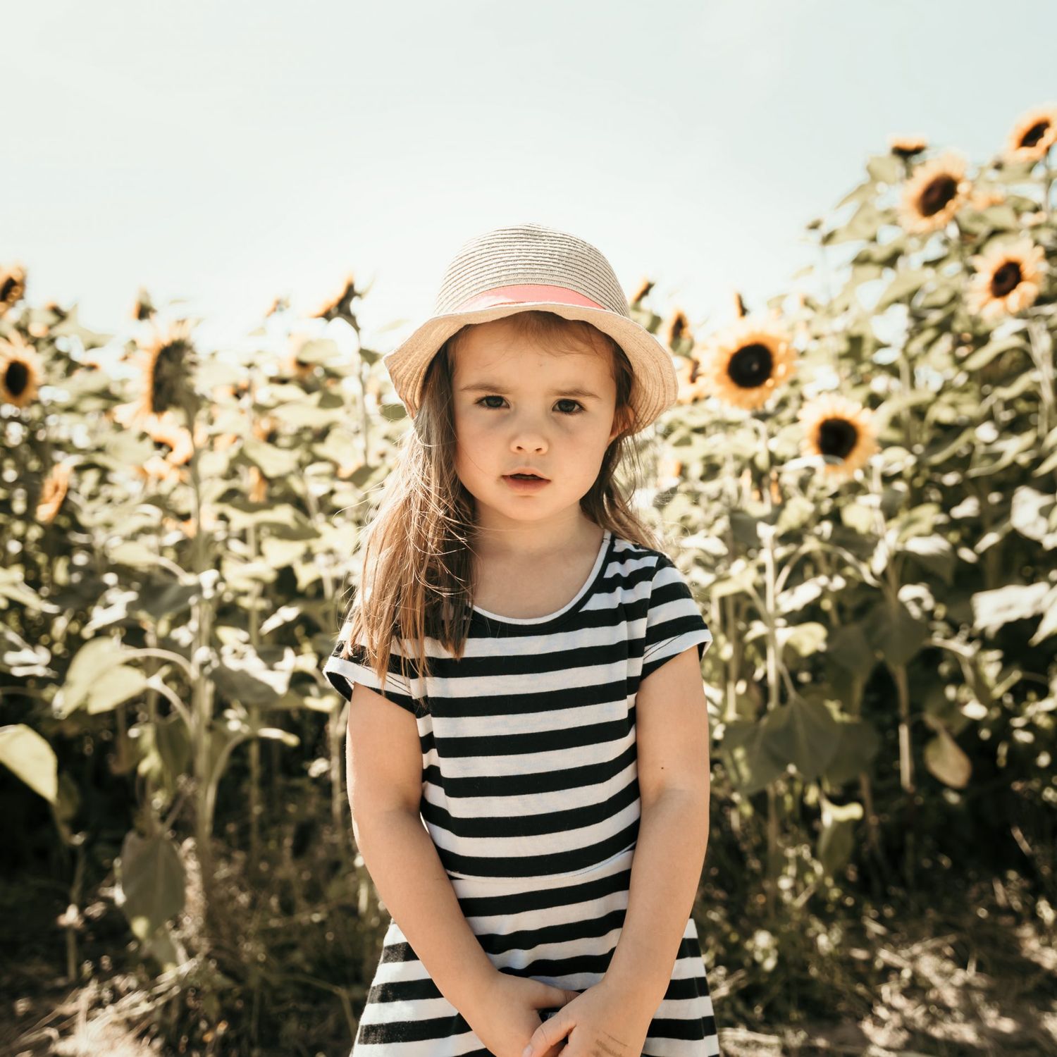 Striped dress and sunhat against backdrop of towering sunflowers in summer garden.