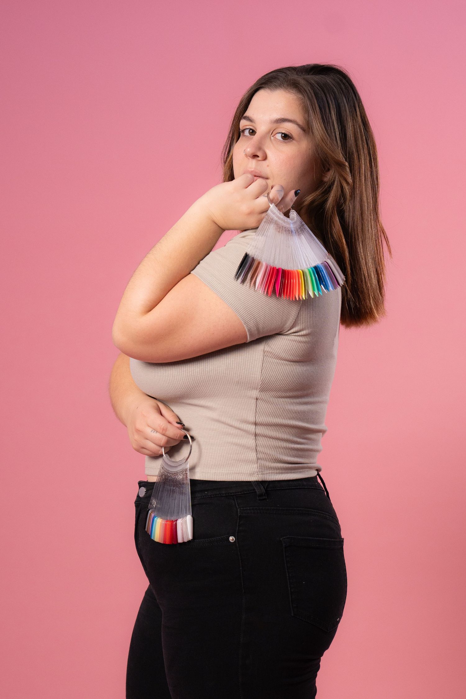 Woman in grey shirt and black pants reveals rainbow colored hair in creative photo sequence against pink background.