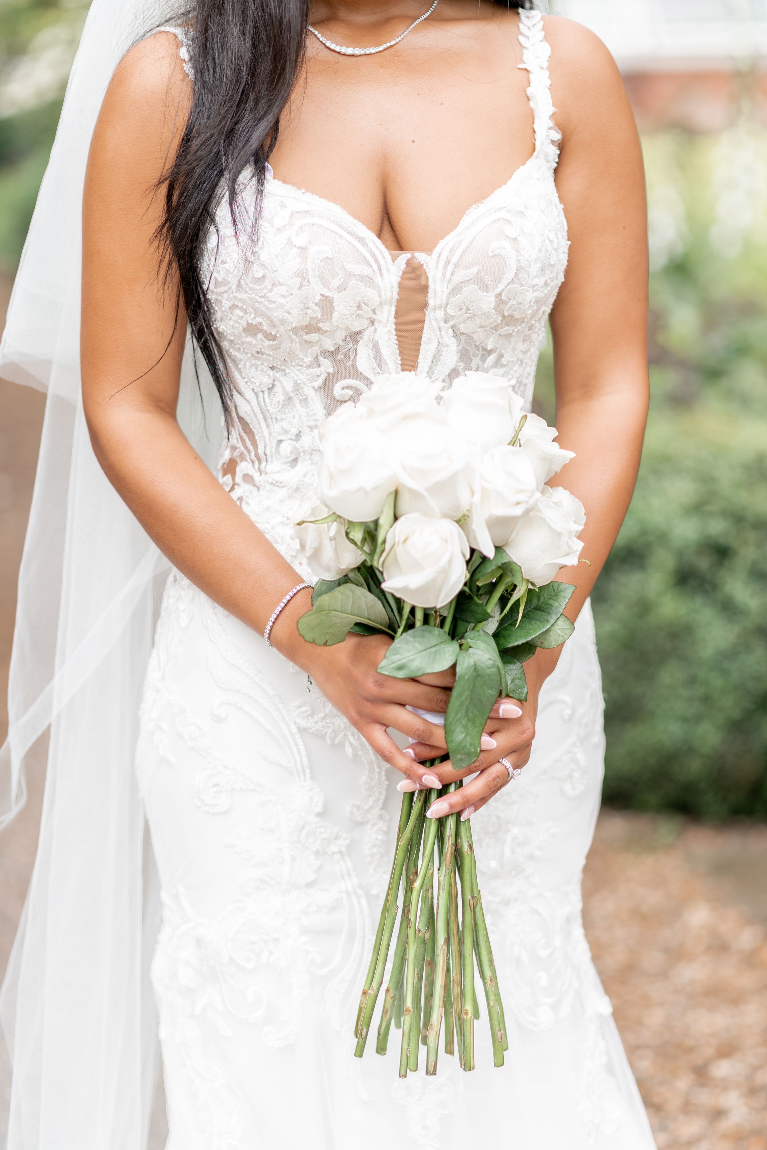 Close-up of a bride in a white lace wedding dress holding a simple bouquet of white roses. Braxted Park.