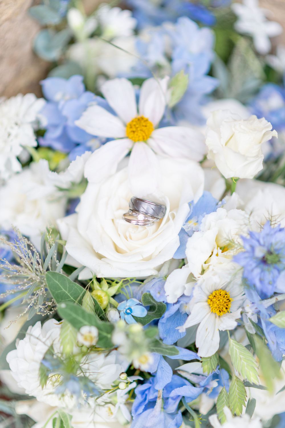Wedding rings nestled in white roses and daisies with delicate blue flowers in a romantic bridal bouquet.