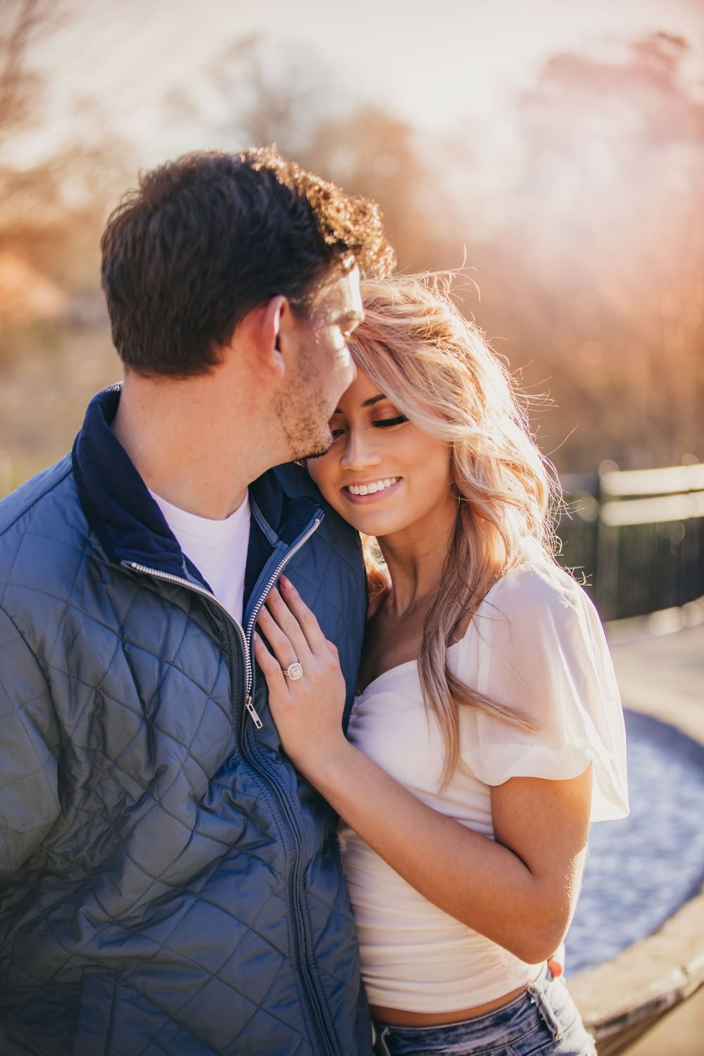 man kisses fiancé's forehead as she leans on his shoulder