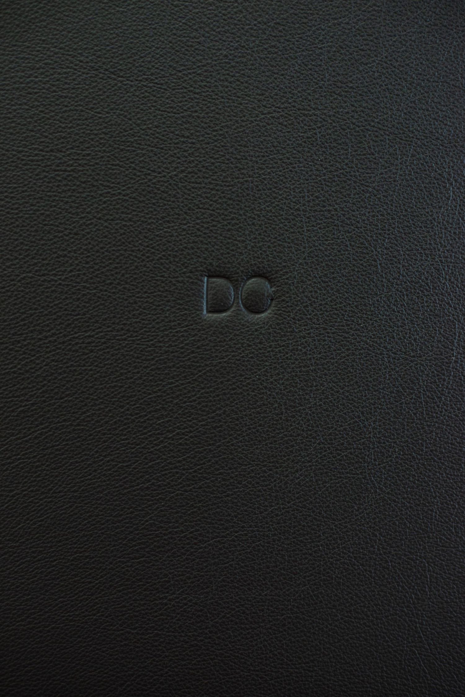 Black leather textured surface with embossed 'DC' letters.