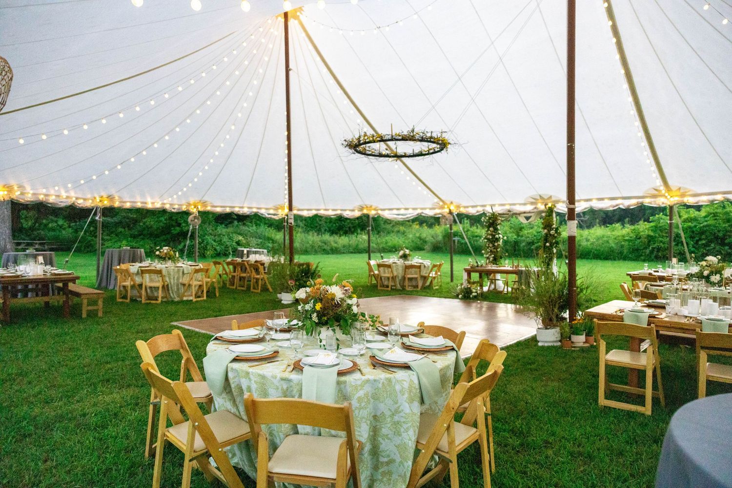Elegant outdoor wedding reception under a sailcloth tent with round tables and floral centerpieces.