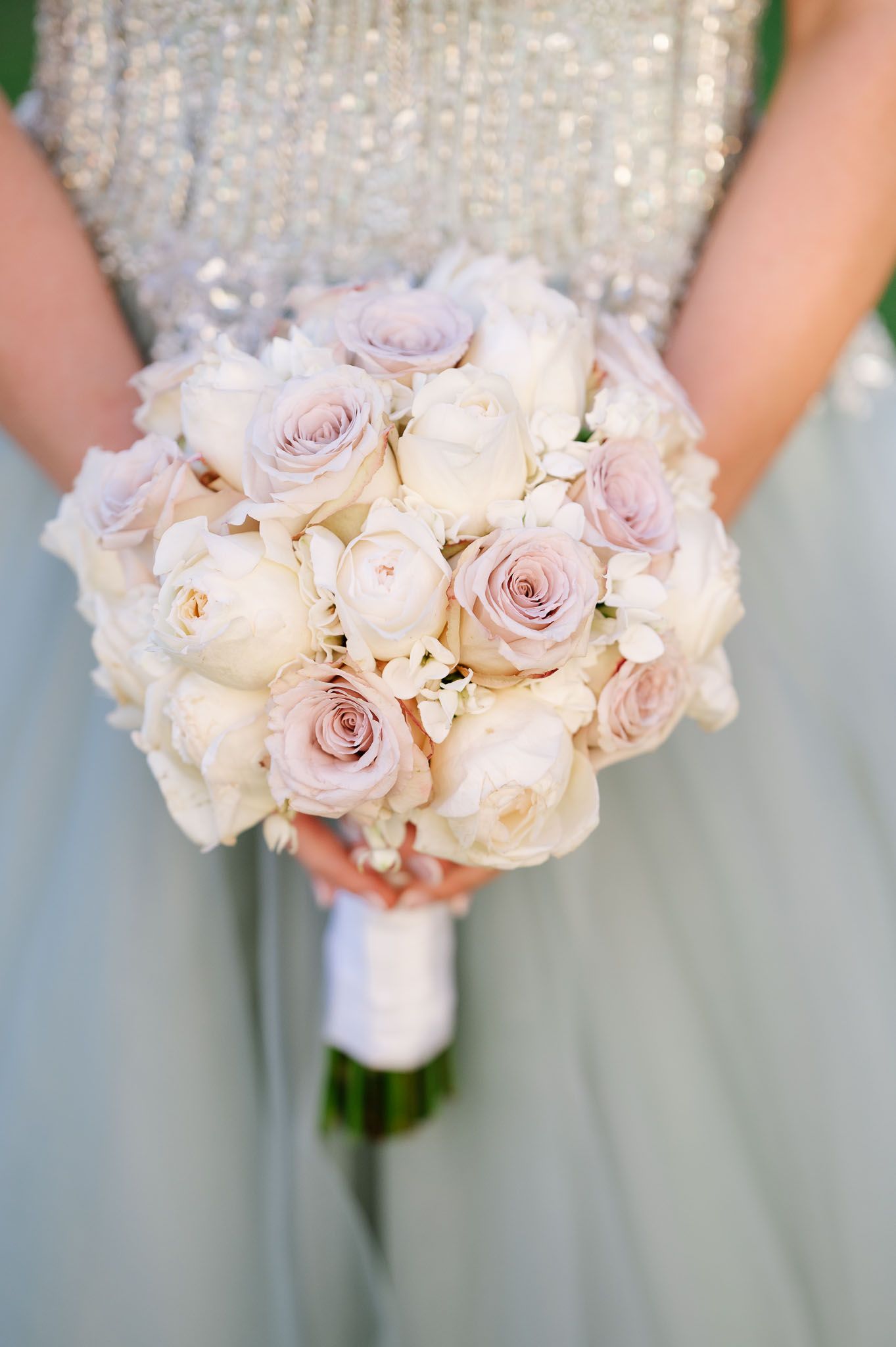 Delicate bridal bouquet of blush and ivory roses wrapped in white ribbon.