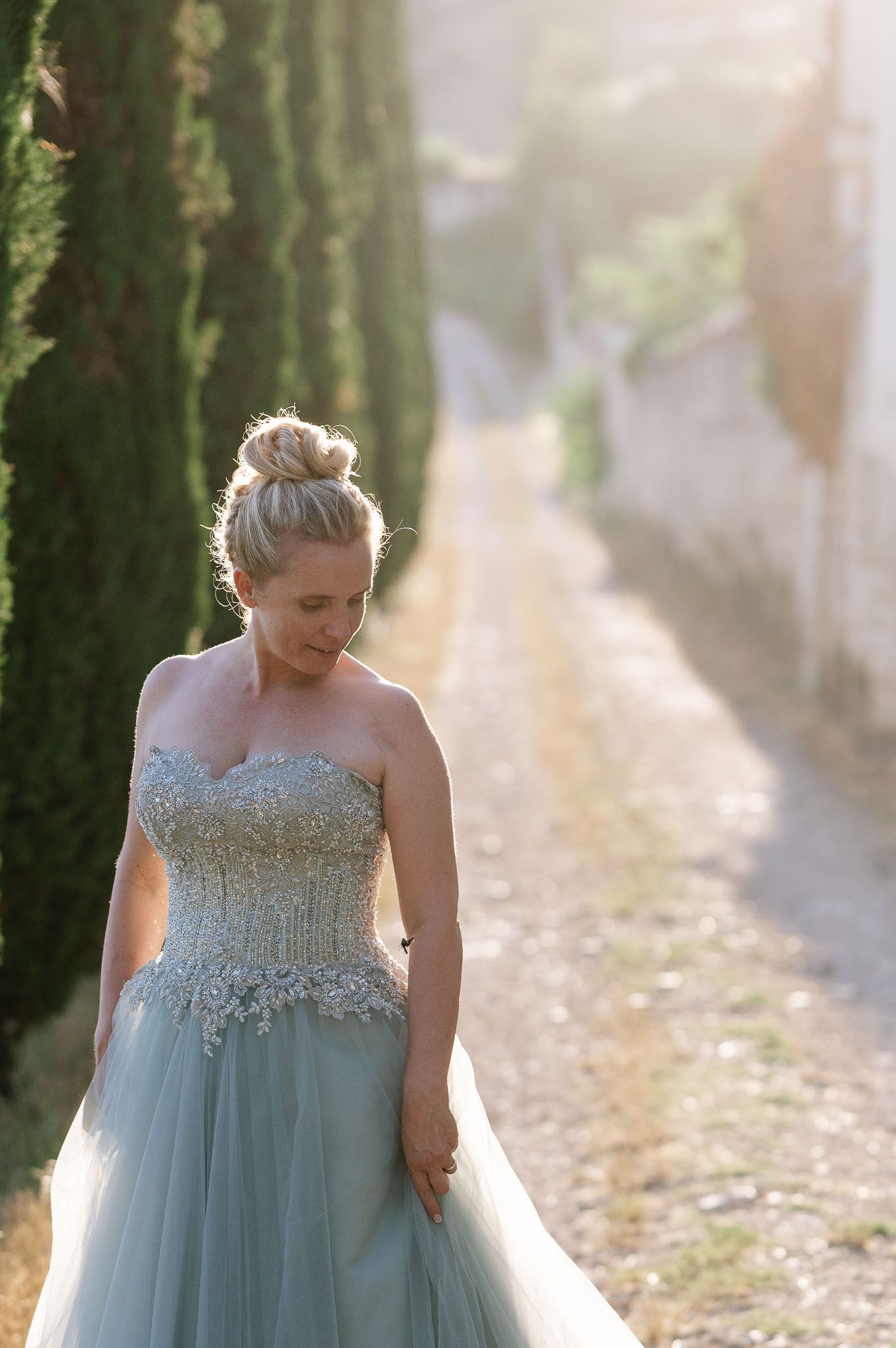 Romantic portrait in soft sunlight among cypress trees featuring a blue wedding gown.