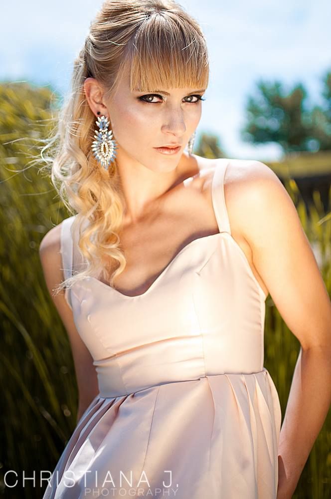 Sunlit portrait in pale pink dress with statement earrings and styled blonde hair.
