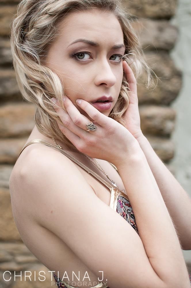 Soft beauty portrait featuring delicate jewelry and natural makeup against stone wall.