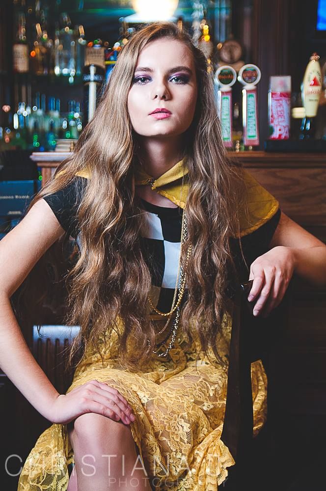 Fashion portrait in bar setting wearing yellow dress with long wavy hair.