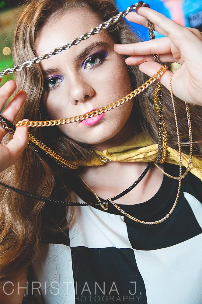 Creative fashion portrait with gold chain accessories against checkered pattern.