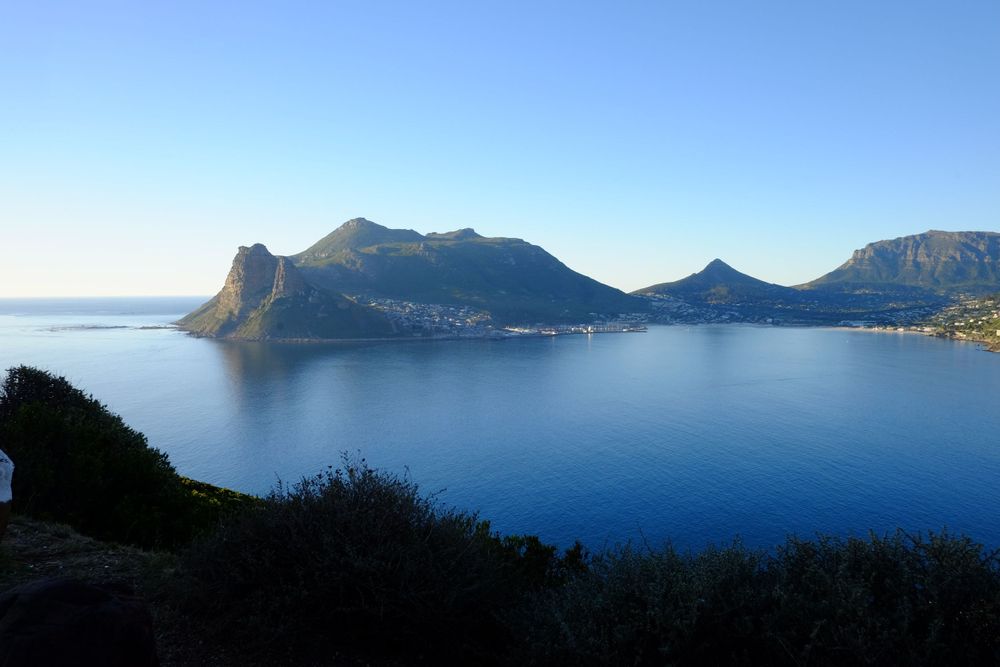 Stunning panoramic view of Hout Bay, South Africa, with mountains reflecting in calm blue harbor waters.