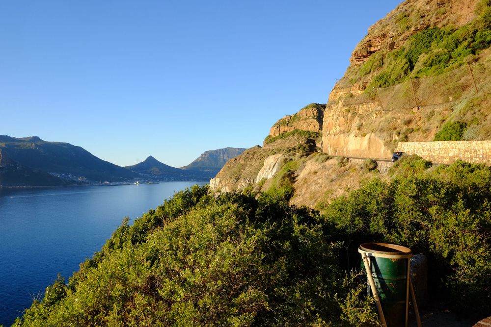 Chapman's Peak Drive clinging to rocky cliffs above a serene blue bay with mountain views beyond.