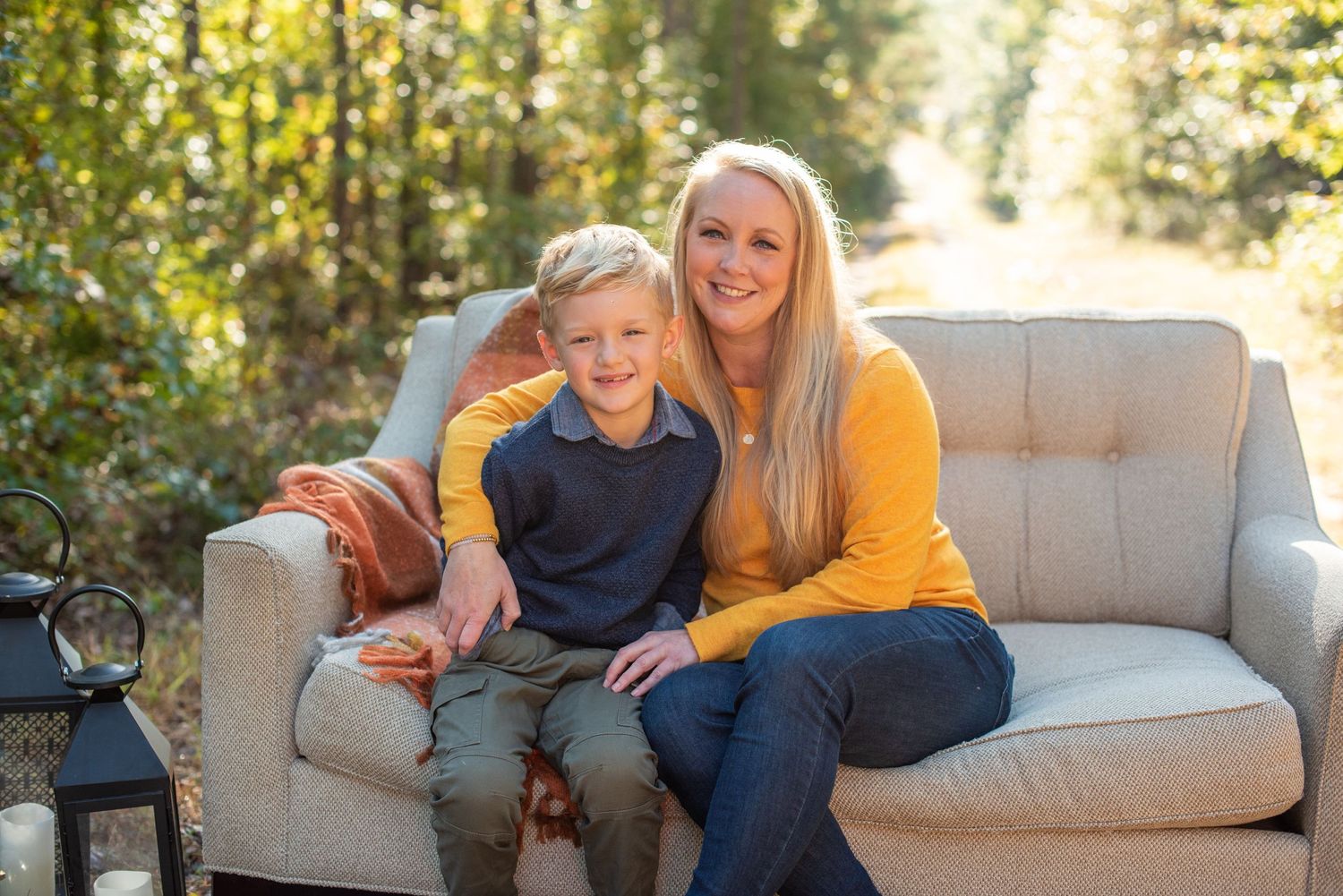 Parent and child sitting together on gray outdoor couch in autumn sunlight.