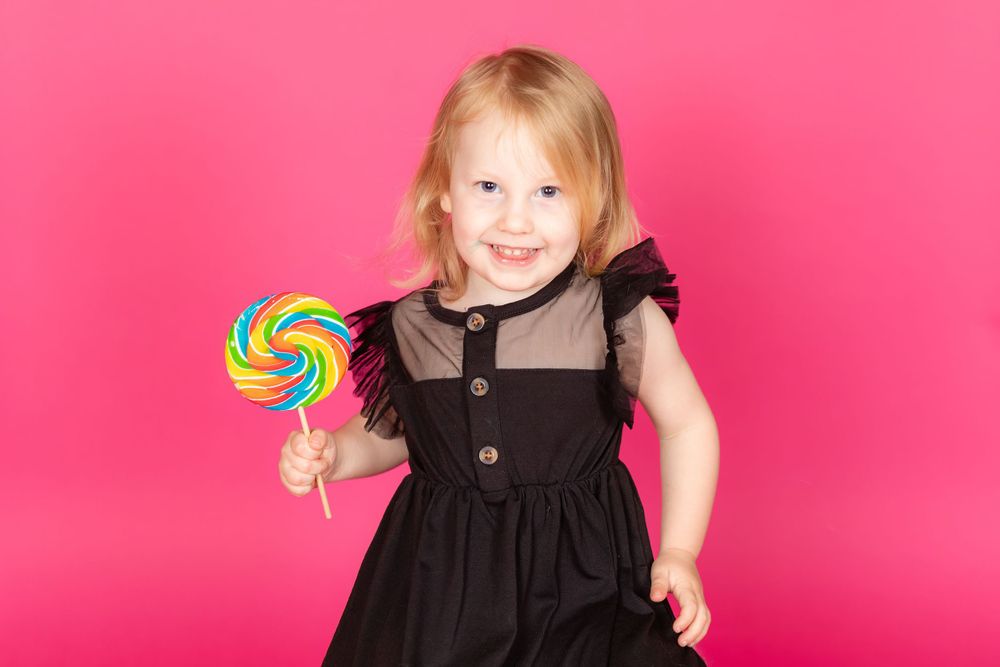 little girl in black dress with bright lollipop on savage tulip pink backdrop in studio clayton new jersey gloucester