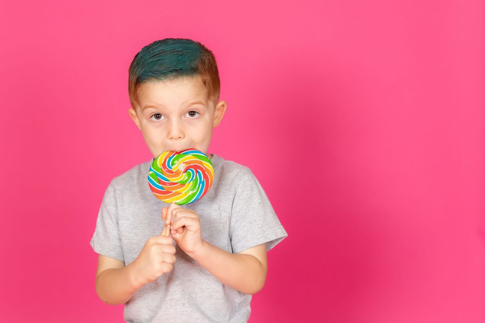 little boy with teal hair with bright lollipop on savage tulip pink backdrop in studio in clayton new jersey Gloucester