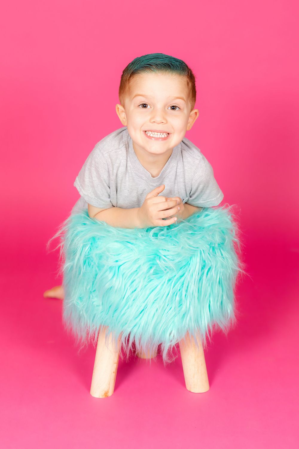 little boy with teal hair leaning on teal stool on savage tulip pink backdrop in studio in clayton new jersey Gloucester
