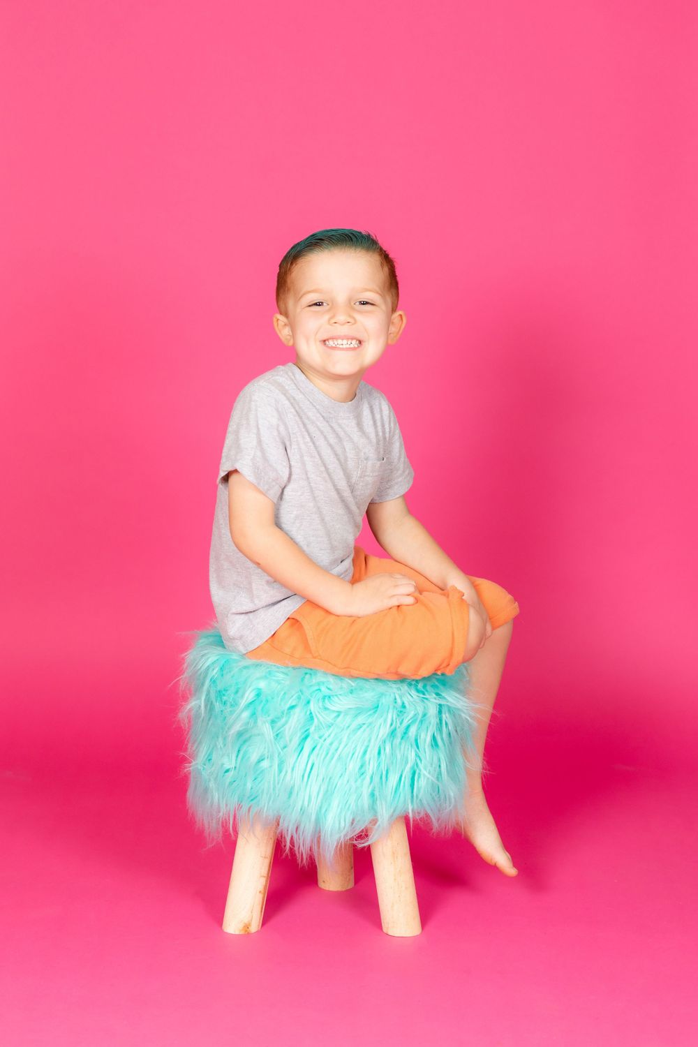 little boy with teal hair leaning on teal stool on savage tulip pink backdrop in studio in clayton new jersey Gloucester